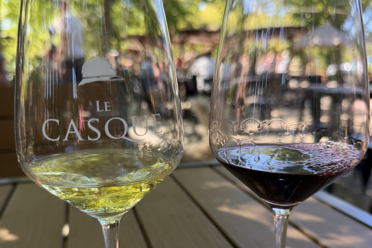 Two wine glasses, one white and one red, on a wooden table on the outdoor patio at Le Casque in Loomis, California. The glass on the left is etched with the Le Casque helmet logo.